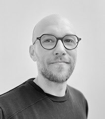 Portrait en noir et blanc de Urb1n, créatif et professionnel, portant des lunettes rondes.