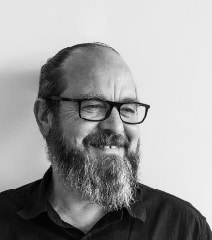 Homme avec lunettes et barbe, souriant, en portrait noir et blanc.