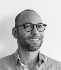 Portrait professionnel en noir et blanc d'un homme souriant portant des lunettes.